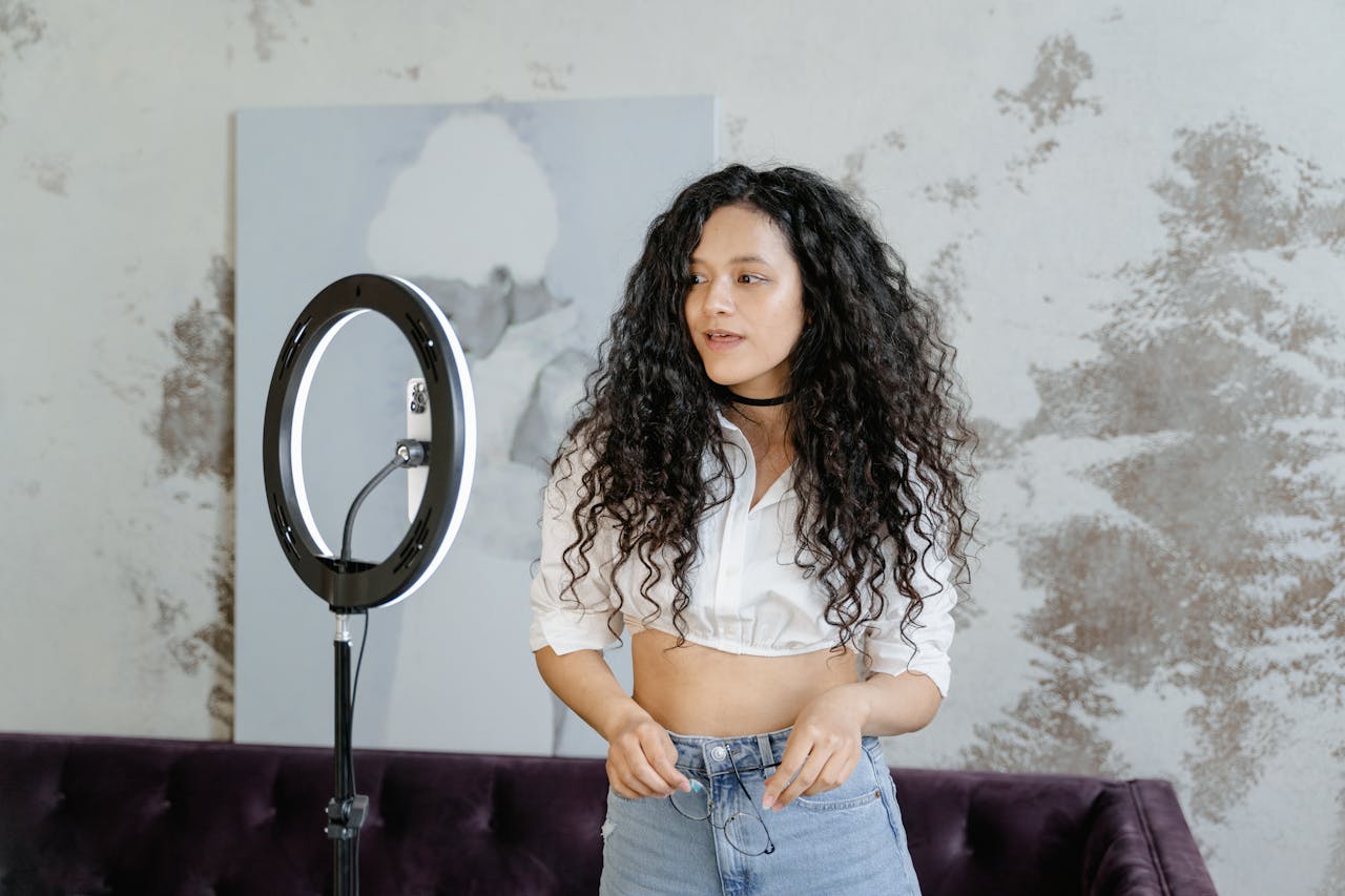 Woman in White Floral Shirt and Blue Denim Jeans Standing Near Round Mirror